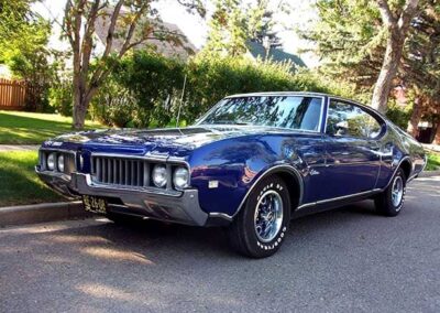 1969 Oldsmobile Cutlass in vibrant blue parked on a tree-lined street, showcasing classic car restoration by Wilson Auto Repair.