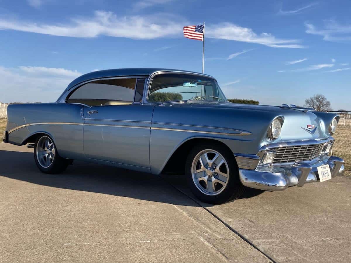 Classic 1956 Chevy Bel Air in blue, showcasing vintage design and chrome accents, with an American flag in the background, relevant to classic car insurance and financing discussions.