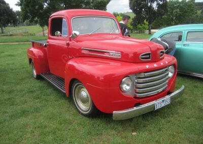 1948 Ford F-1 pickup truck in vibrant red, showcasing classic car restoration by Wilson Auto Repair, parked on grass with trees in the background.